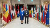 Mme Simon Beissel et M. Dan Hardy avant les drapeaux des Etats participants