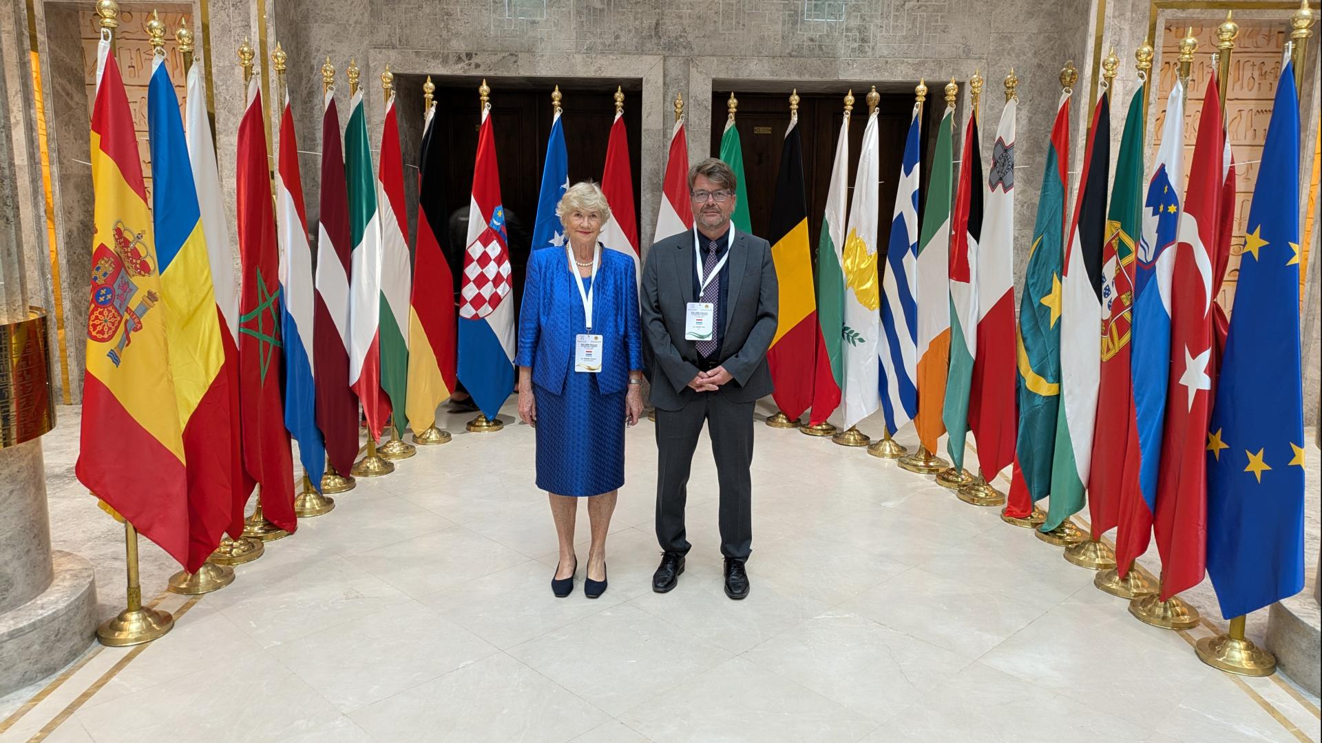 Mme Simon Beissel et M. Dan Hardy avant les drapeaux des Etats participants